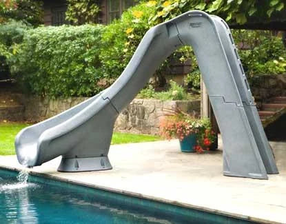 Pool slide attached to a pool with a garden and stone wall in the background