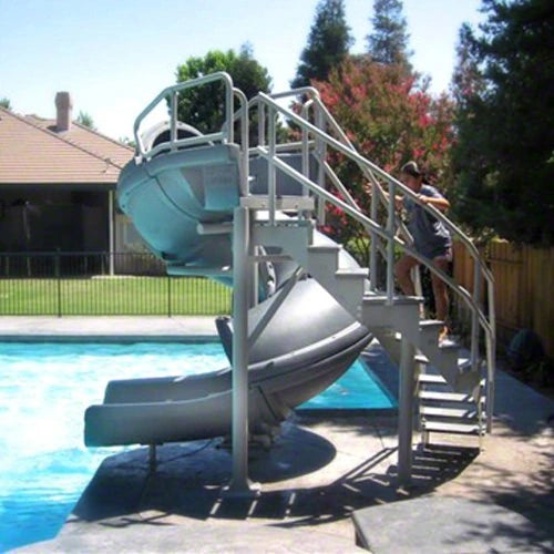 Swimming pool with a slide and staircase, surrounded by trees and a house.